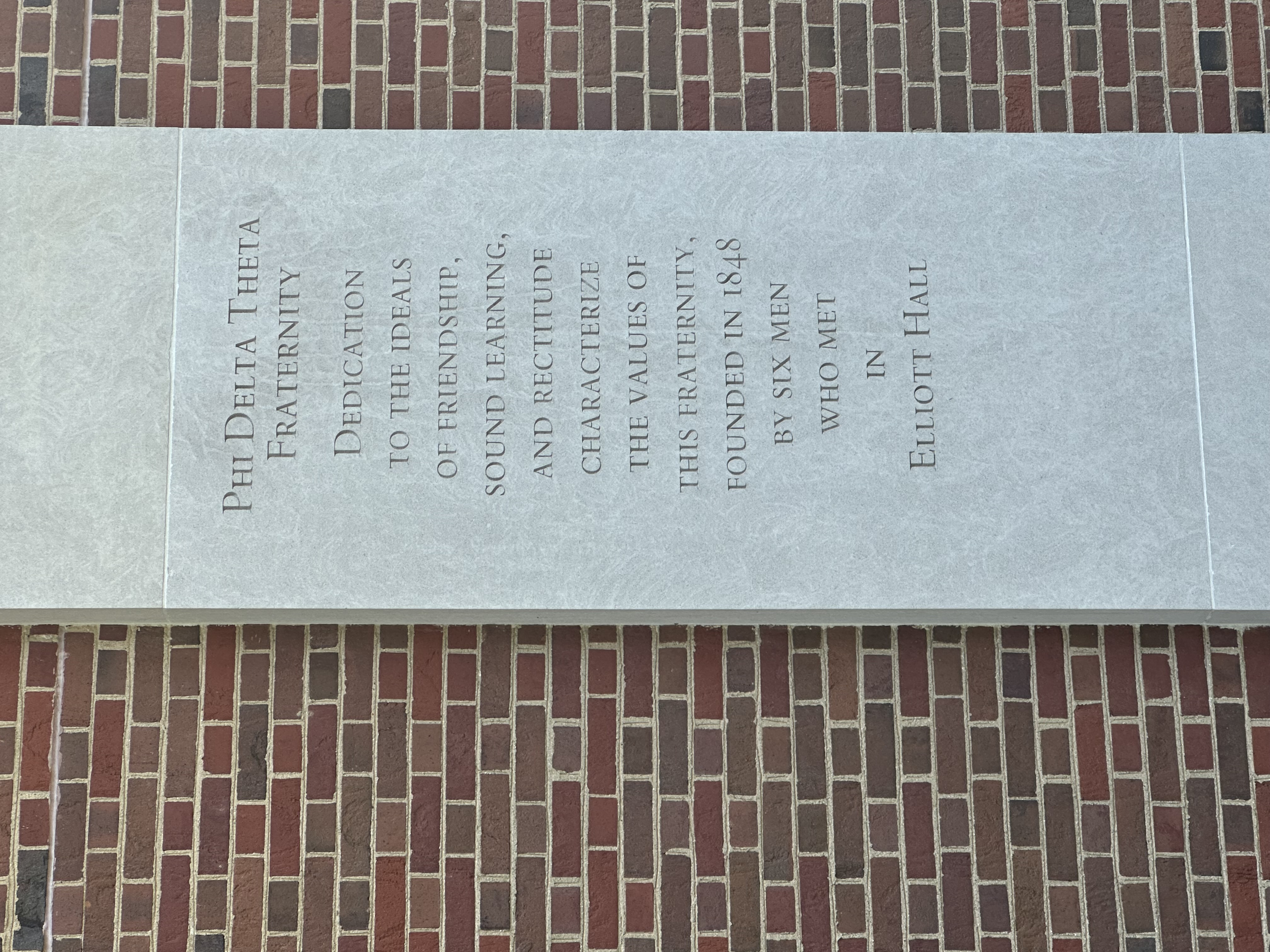 A commemorative plaque on the side of the auditorium amongst other commemorative plaques for different greek life societies